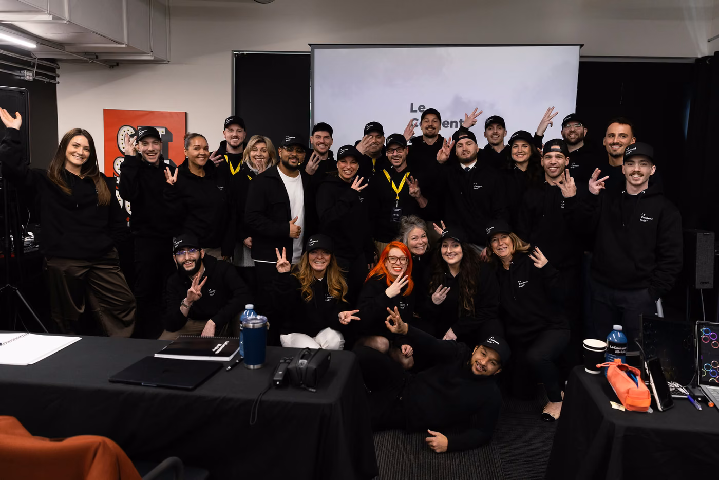 Photo de groupe d'une cohorte d'une trentaine de personnes, doigts levés vers l'objectif, devant l'écran de la salle