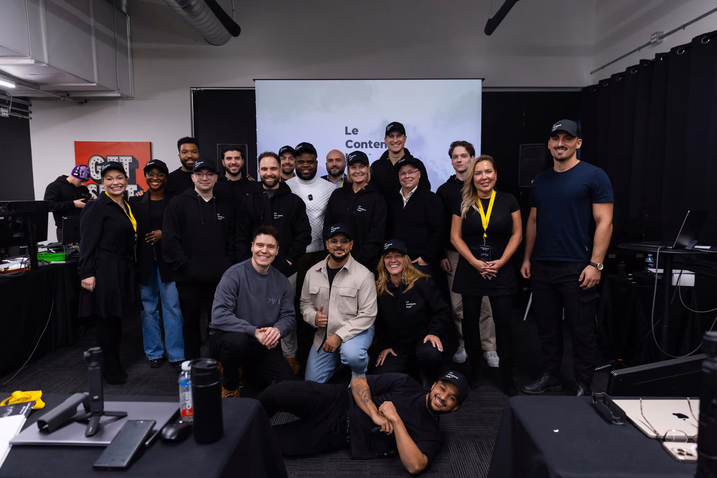 Photo de groupe d'une cohorte dans le studio, une vingtaine de personnes debout et accroupies devant l'écran de présentation